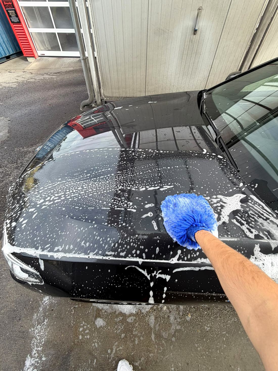 Eingeschäumte Motorhaube wird mit dem Waschhandschuh gewaschen